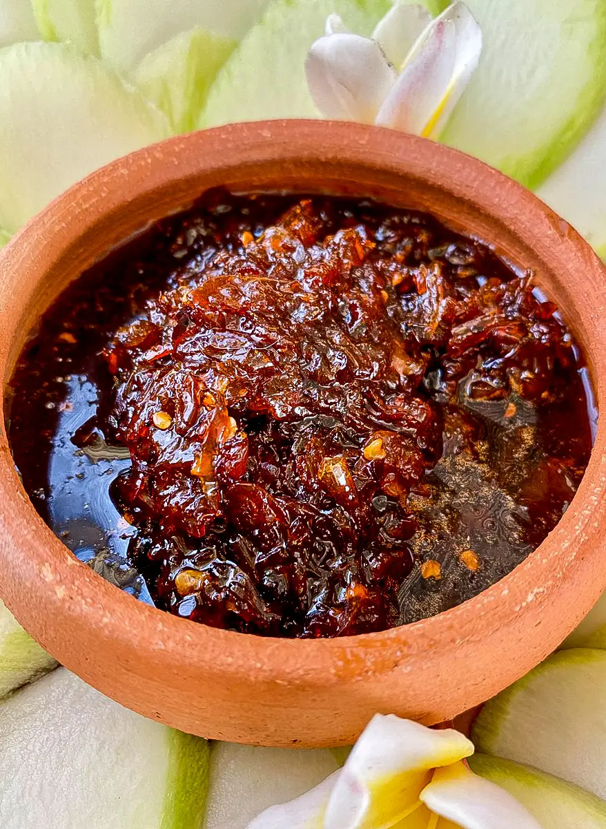 Thai mango dipping sauce in a clay sauce cup, with parts of green mango spread around it.