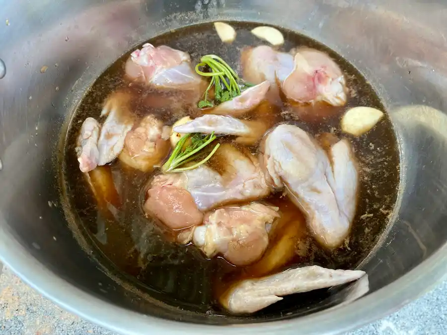 A cooking pot with chicken wings, Coca-Cola, and herbs in a single layer.