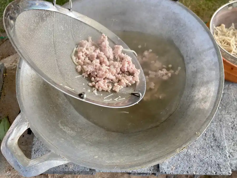 Cooking pork meat in a large aluminum wok.