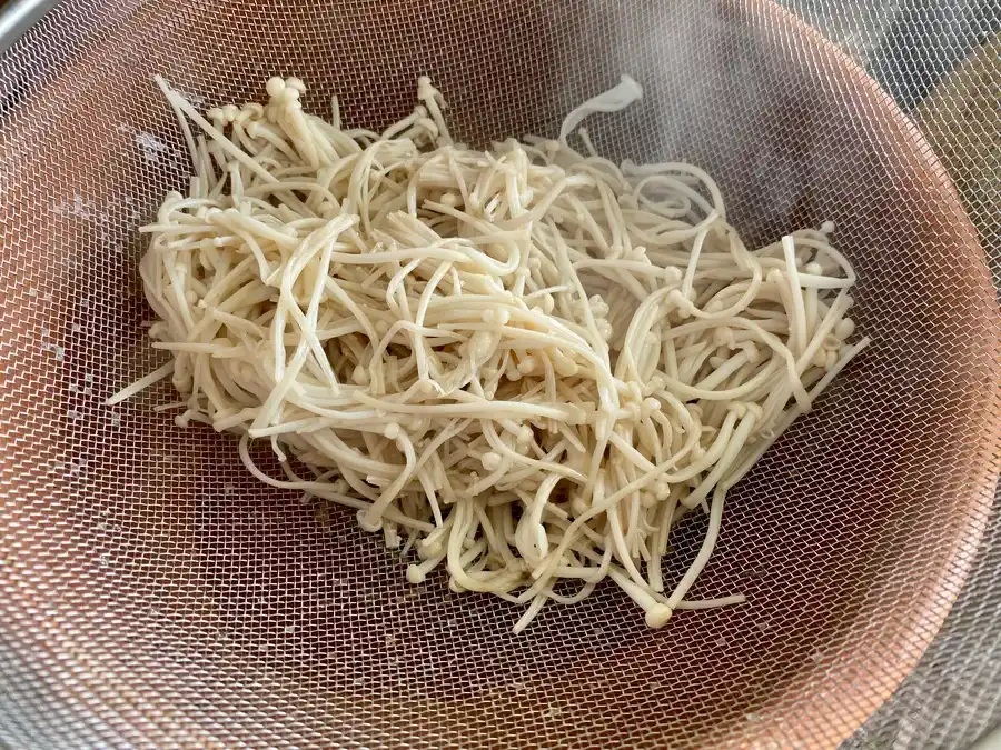 Enoki mushrooms on top of a sieve in a clay pot.