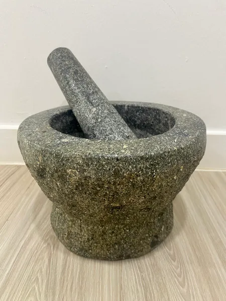 A granite mortar and pestle set on a wooden floor in front of a white wall.