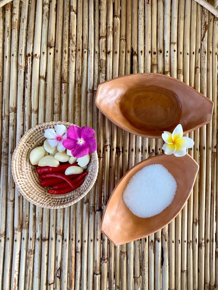 Ingredients for Thai spicy vinegar dipping sauce, fresh red chilies, garlic, and white sugar, laid out in terracotta bowls on a bamboo mat.