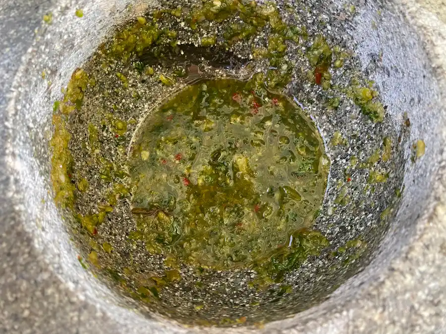 A green dipping sauce named nam jim seafood in a stone mortar and pestle.
