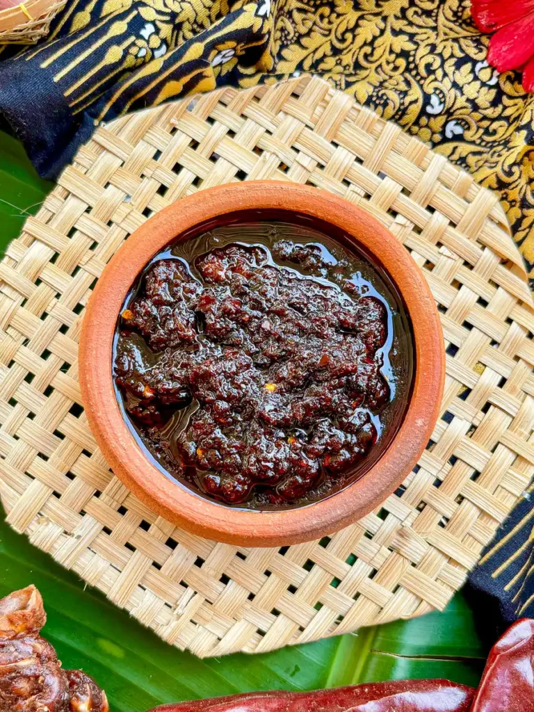 Nam prik pao, Thai chili paste, in clay cup with chilies, garlic, and shallots scattered around.