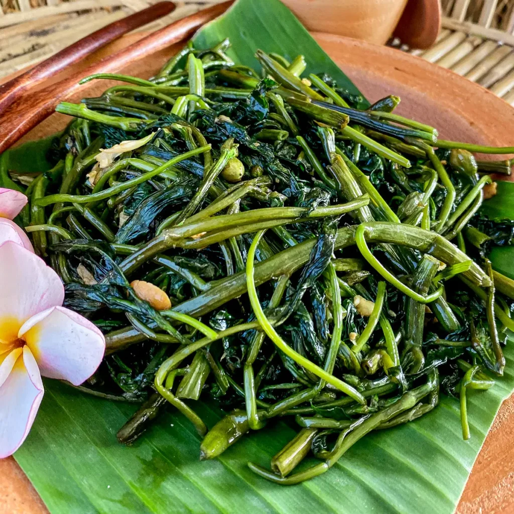 Close-up of pad pak boong, glistening stir-fried morning glory with green stems and wilted leaves.