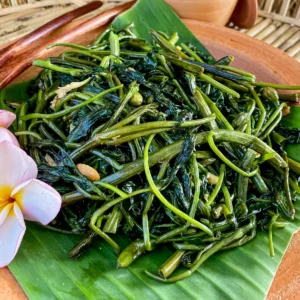 Close-up of pad pak boong, glistening stir-fried morning glory with green stems and wilted leaves.