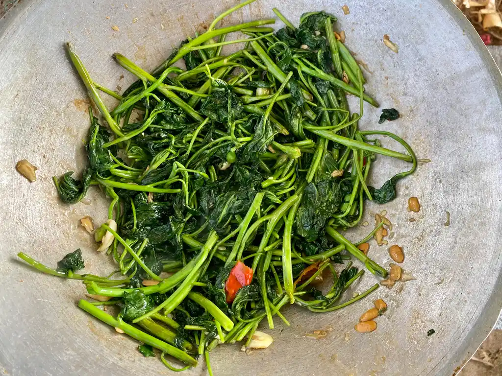 Stir-fried pad pak boong (morning glory) glistening in a rustic pan.