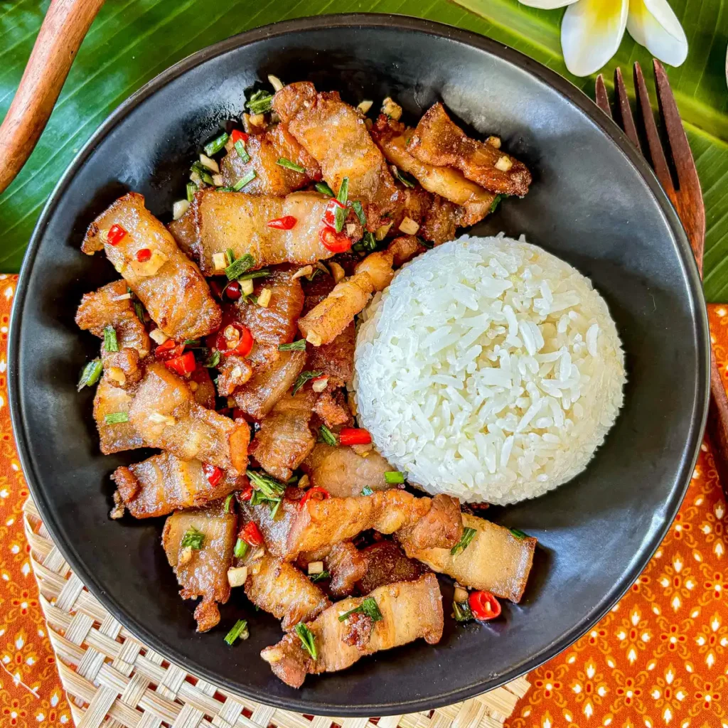 Pork belly chili garlic stir-fry with jasmine rice on a black plate.