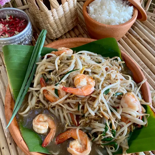 Shrimp with bean sprouts stir-fry in a clay dish, a portion of white rice, and flowers as decorations.