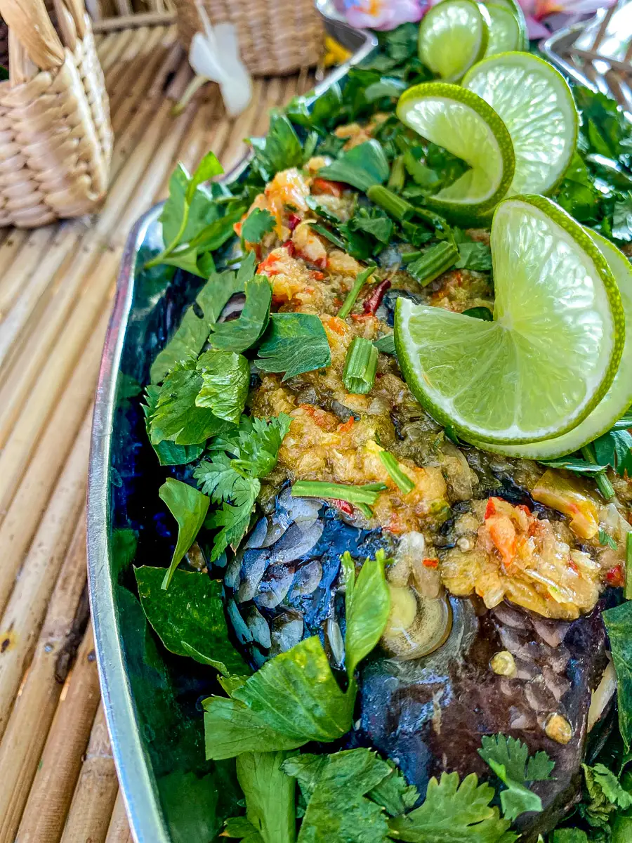 Close-up of Thai lime garlic steamed fish topped with fresh herbs and a spicy sauce.