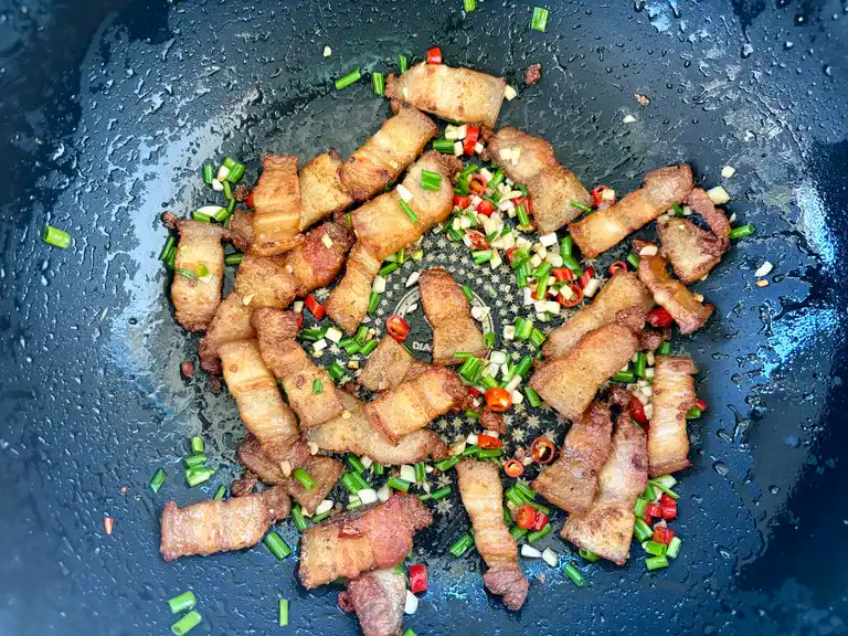 Stir-fried pork belly with garlic and chilies, finished with green onions.