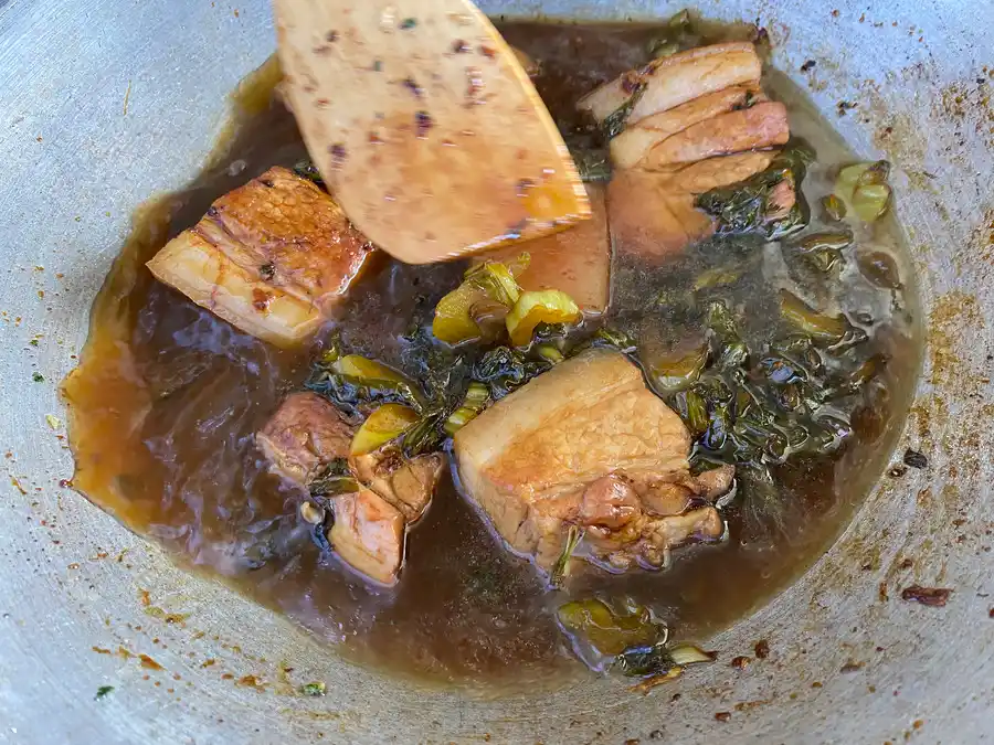 A dark liquid with pork bellyand pickled Chinese cabbage in a wok.