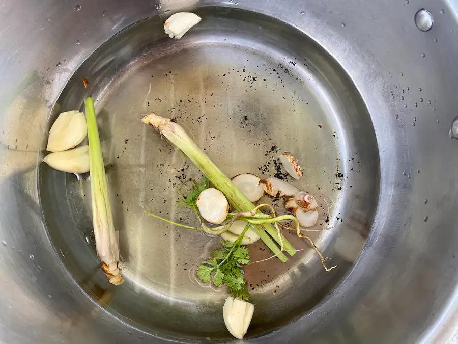 Thai aromatics including garlic, lemongrass, coriander root, and galangal in a pot.