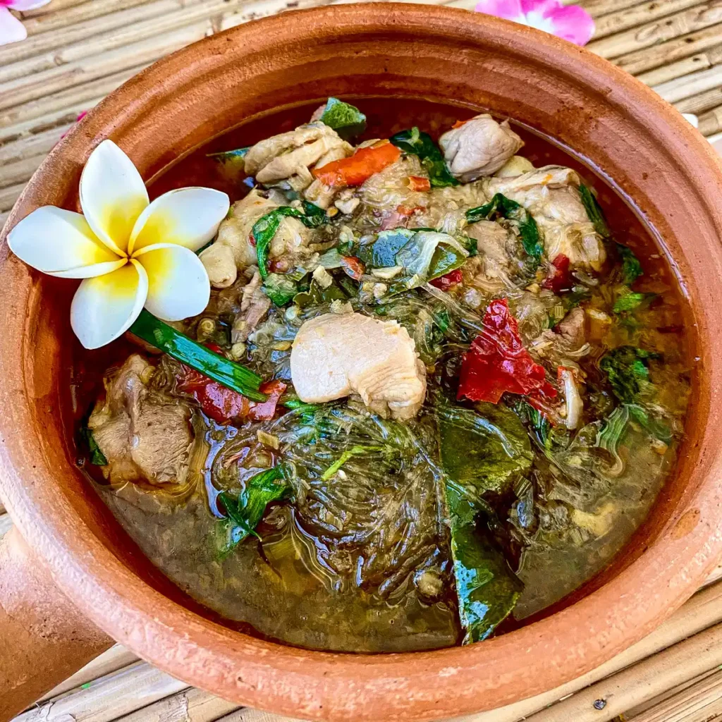 Thai chicken glass noodle soup with red chilies, fresh herbs, and a flower.