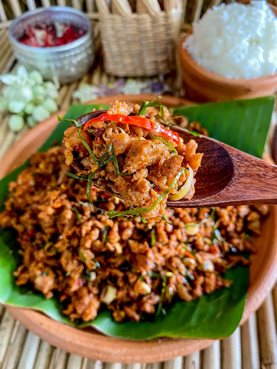 Spoonful of Thai dry mince curry, khua kling, held over a clay dish.