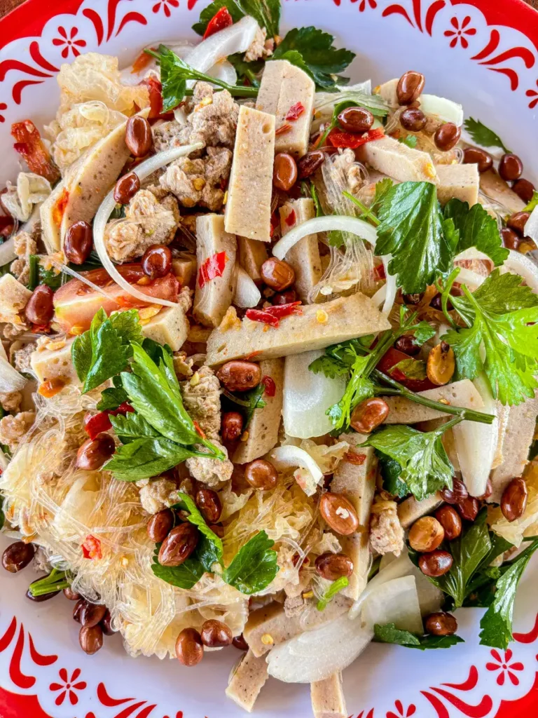 Close-up of Thai yum woon sen salad with glass noodles, ground pork, tofu slices, peanuts, fresh herbs, and a tangy chili dressing.