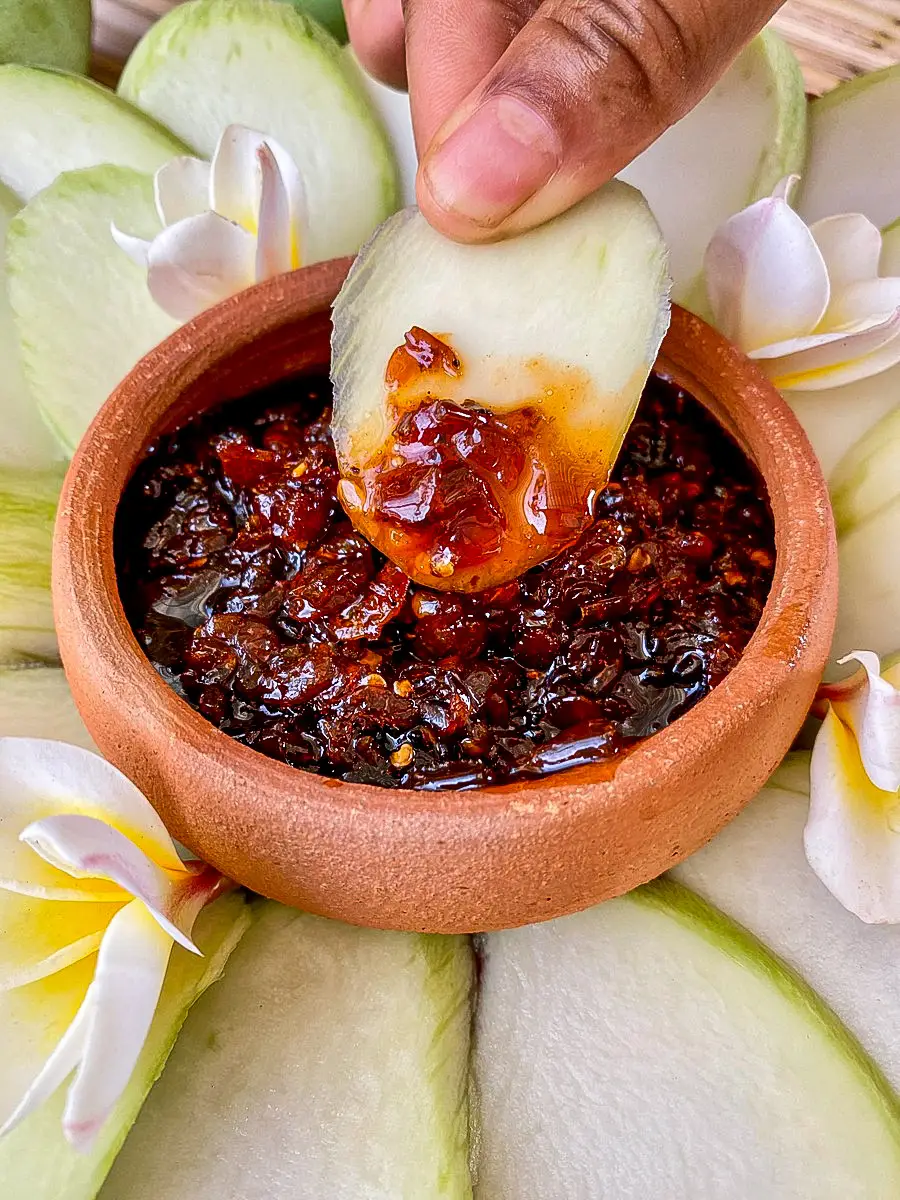 Hand dipping mango slice in Thai green mango dipping sauce.