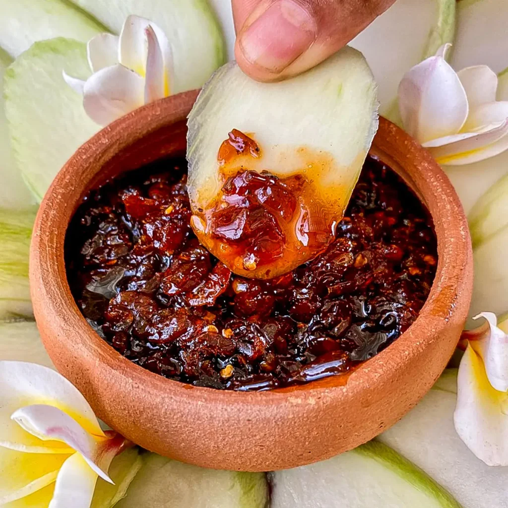 Thai mango dipping sauce in a clay sauce cup, with parts of green mango spread around it.