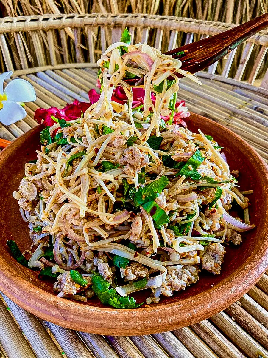Chopsticks lifting Thai mushroom larb made with enoki mushrooms and fresh herbs.