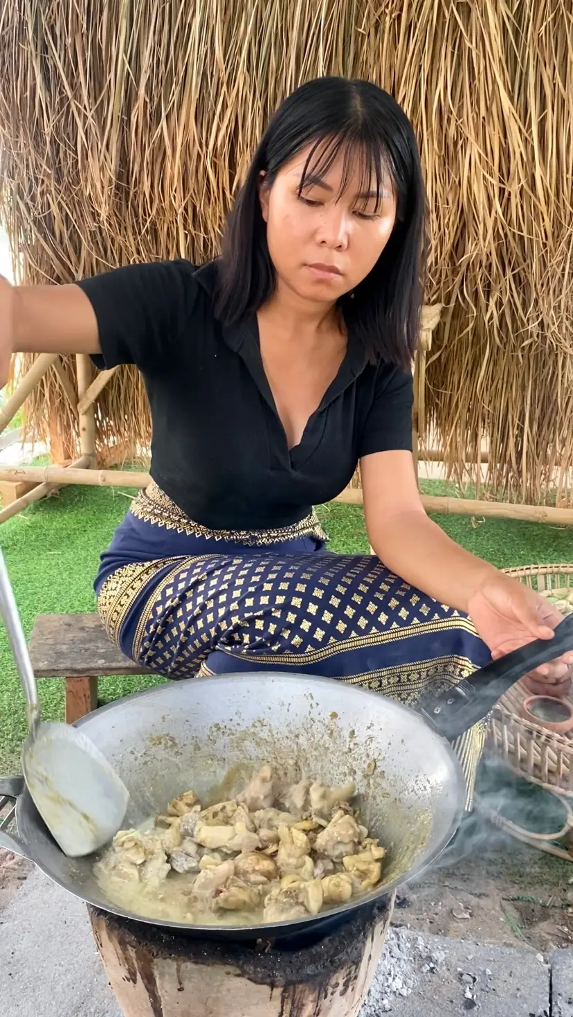 Thai woman making green curry stir-fry in a wok.