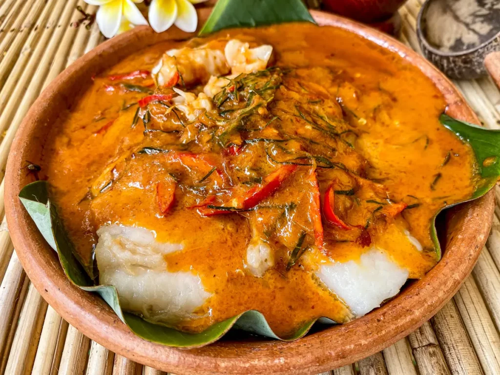 Thai red curry fish with chunks of soft white fish, red chili strips, and herbs in a rustic earthenware bowl.