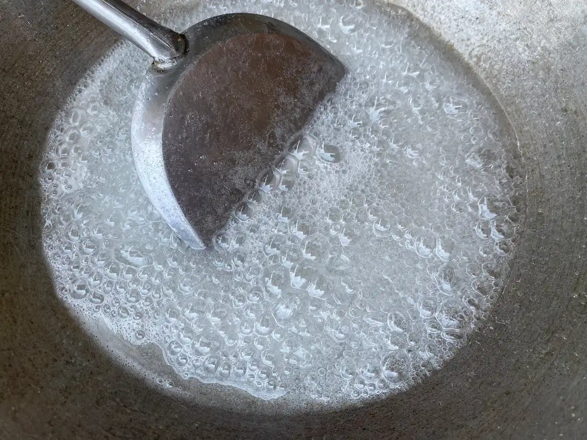 Overhead view of boiling vinegar, white sugar, and salt with a spatula in a wok.