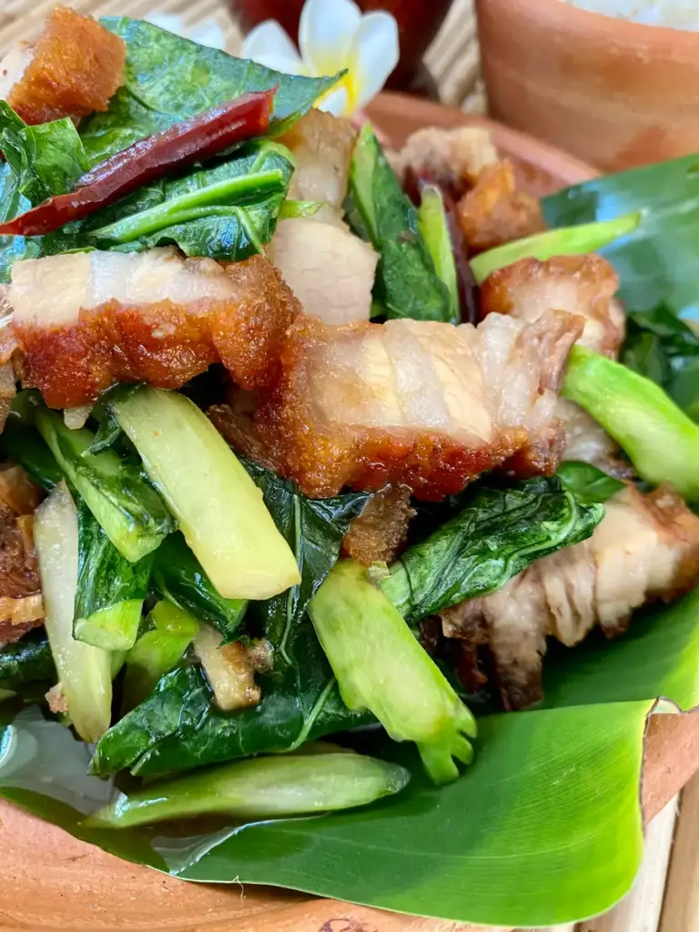 Crispy pork belly with Chinese broccoli served in a clay dish.
