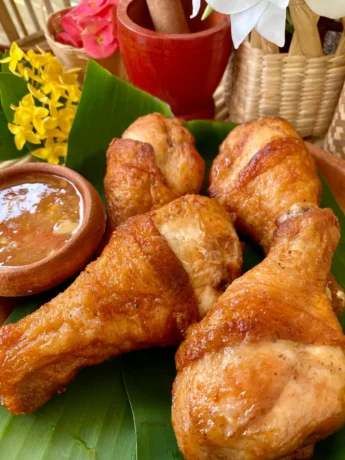 Golden crispy deep-fried chicken drumsticks served on a banana leaf with dipping sauce.