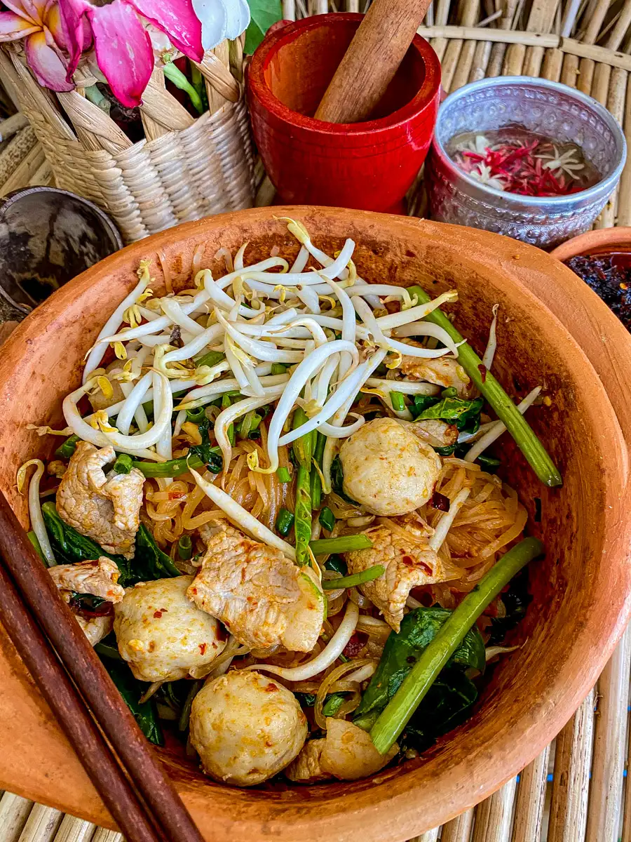 Top-view of dry tom yum noodles in a clay bowl with chopsticks;
