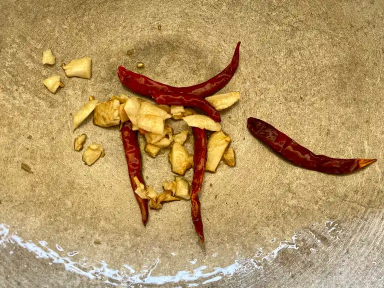 Aromatic garlic and dried chilies being fried to a golden hue in a wok.