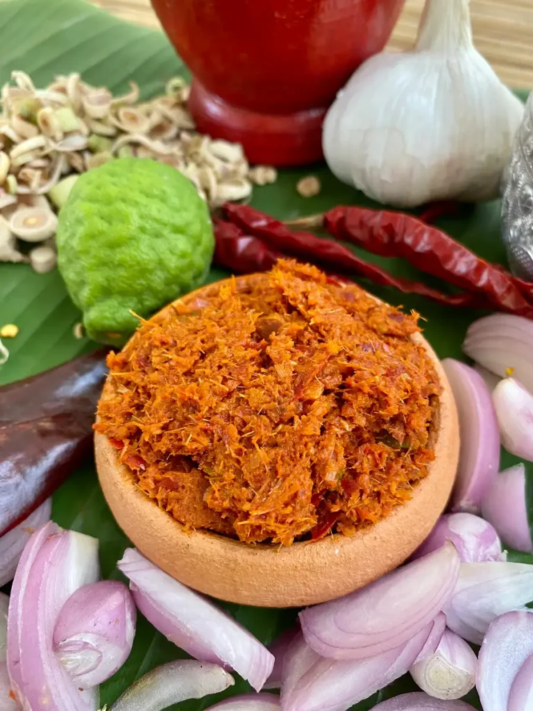 Homemade Thai red curry paste for a vegetarian mortar and pestle recipe, surrounded by fresh vegetables and spices.