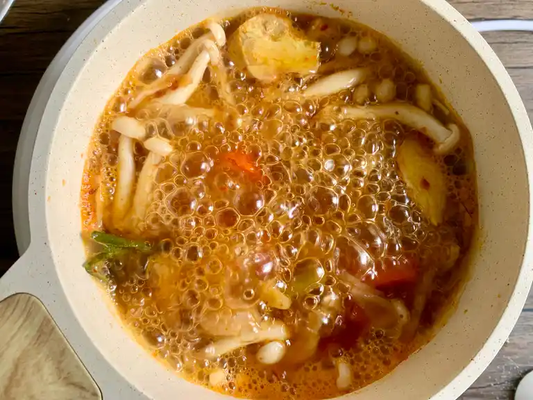 Enoki mushrooms and aromatics simmering in spicy and creamy tom yum soup.