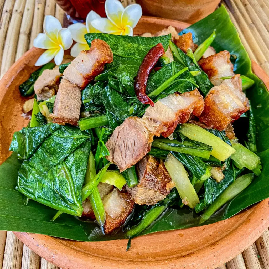 Close-up of pad kana moo krob, crispy pork belly with kale stir-fry, highlighting texture and colors.
