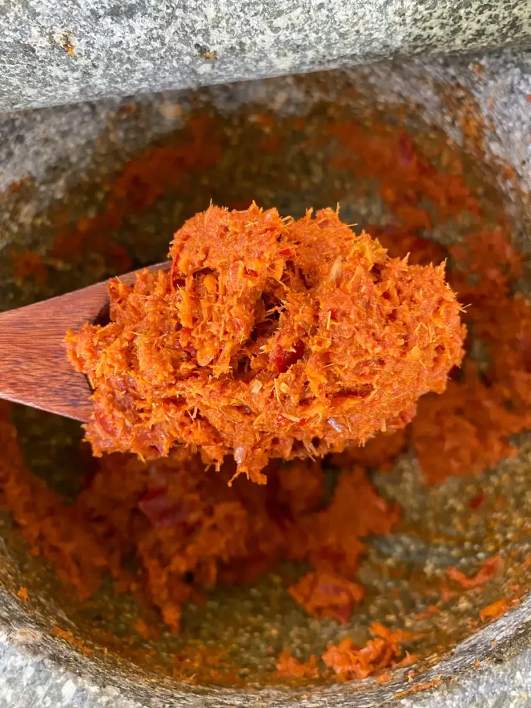 Close-up of Thai red curry paste in a wooden spoon over a granite mortar.