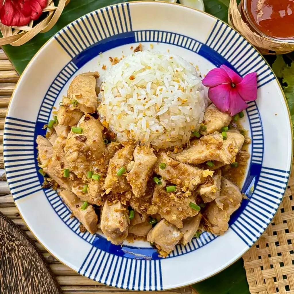 Thai garlic pepper chicken stir-fry served with steamed jasmine rice and garnished with fried garlic and fresh herbs.