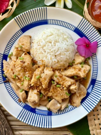 Thai garlic pepper chicken stir-fry, gai pad kratiem prik Thai, presented with jasmine rice and a side of spicy sauce.