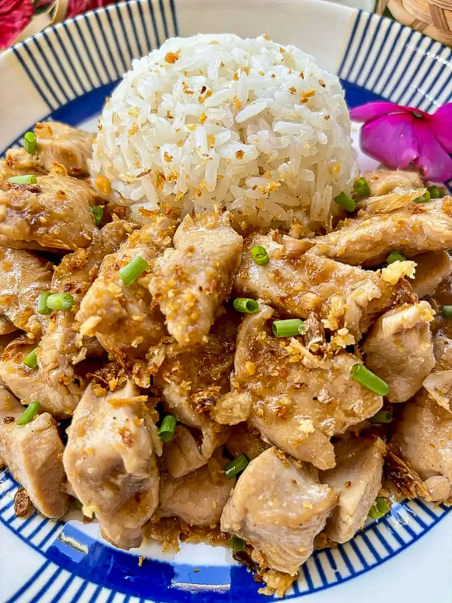 Close-up of Thai garlic pepper chicken with golden garlic topping and fluffy white rice, served on a patterned ceramic plate.