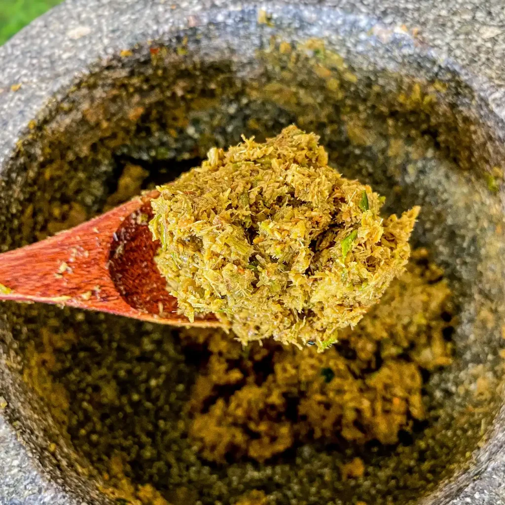 Thai green curry paste held in a wooden spoon over a mortar.