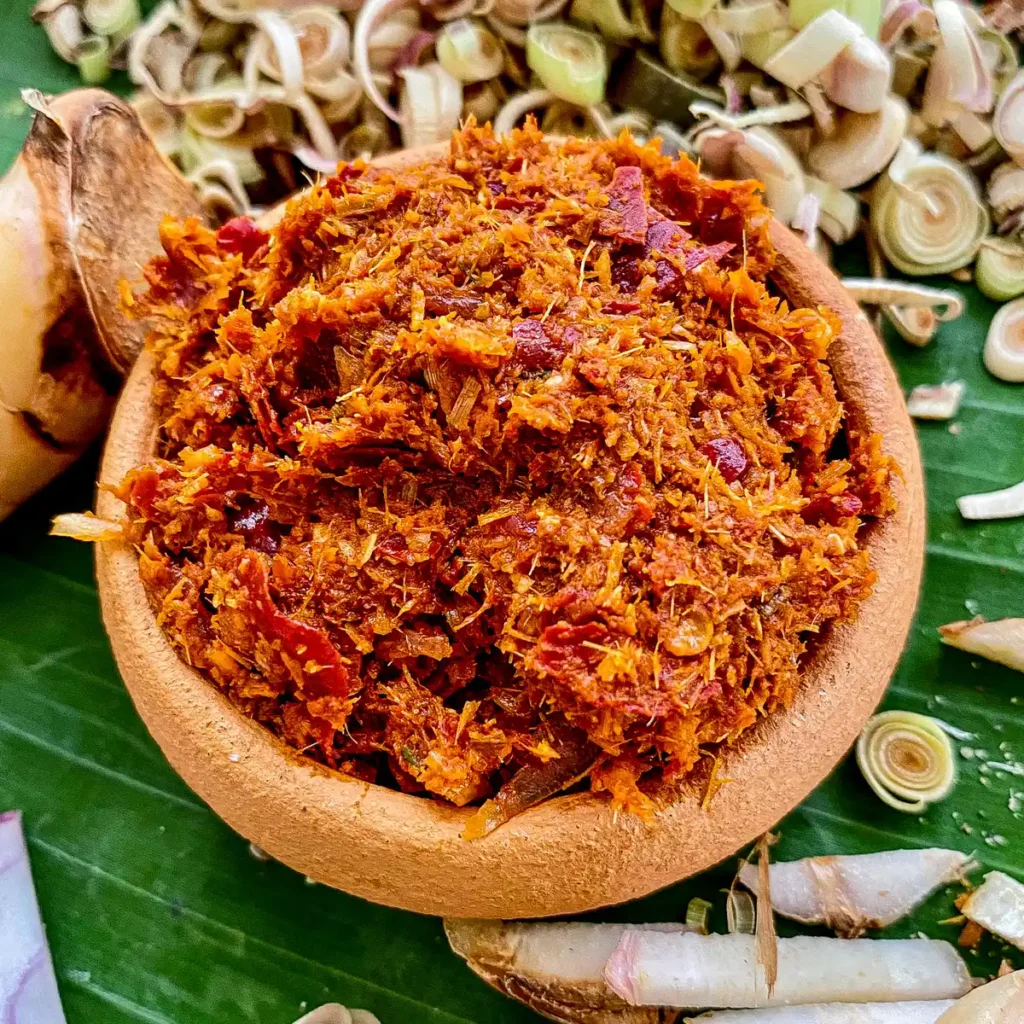 Homemade Thai panang curry paste in a clay bowl, packed with dried chilies, lemongrass, galangal, and aromatic herbs on a banana leaf background.