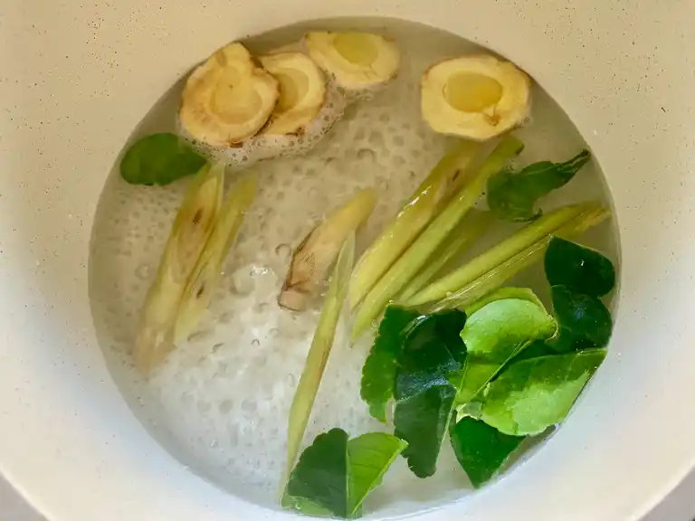 Galangal, lemongrass, and kaffir lime leaves boiling in water.