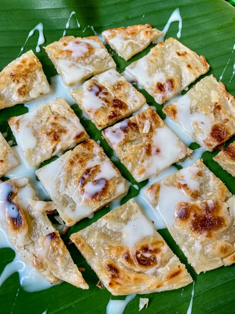 Crispy Thai roti sliced into squares and drizzled with sweetened condensed milk, served on a banana leaf.