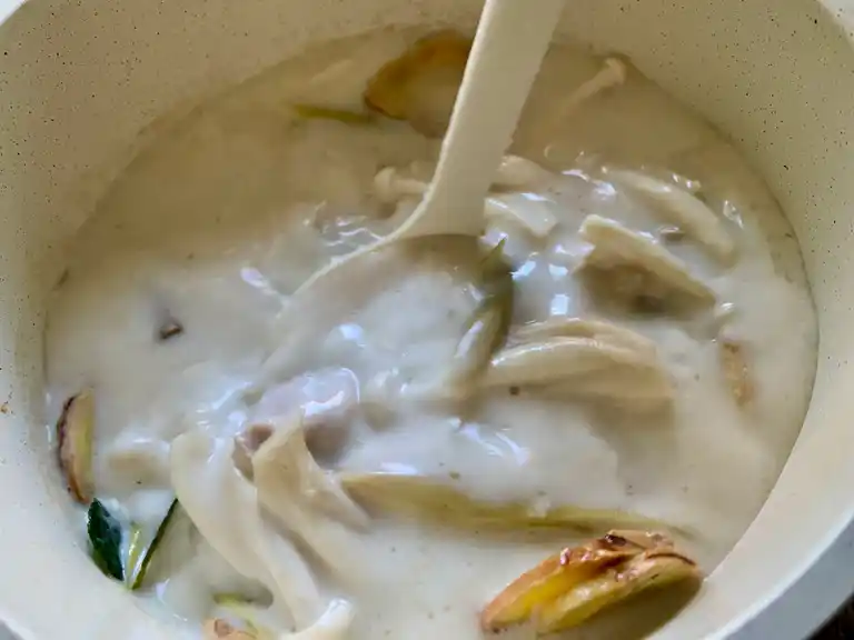 Coconut milk being stirred into the soup with aromatic Thai herbs.