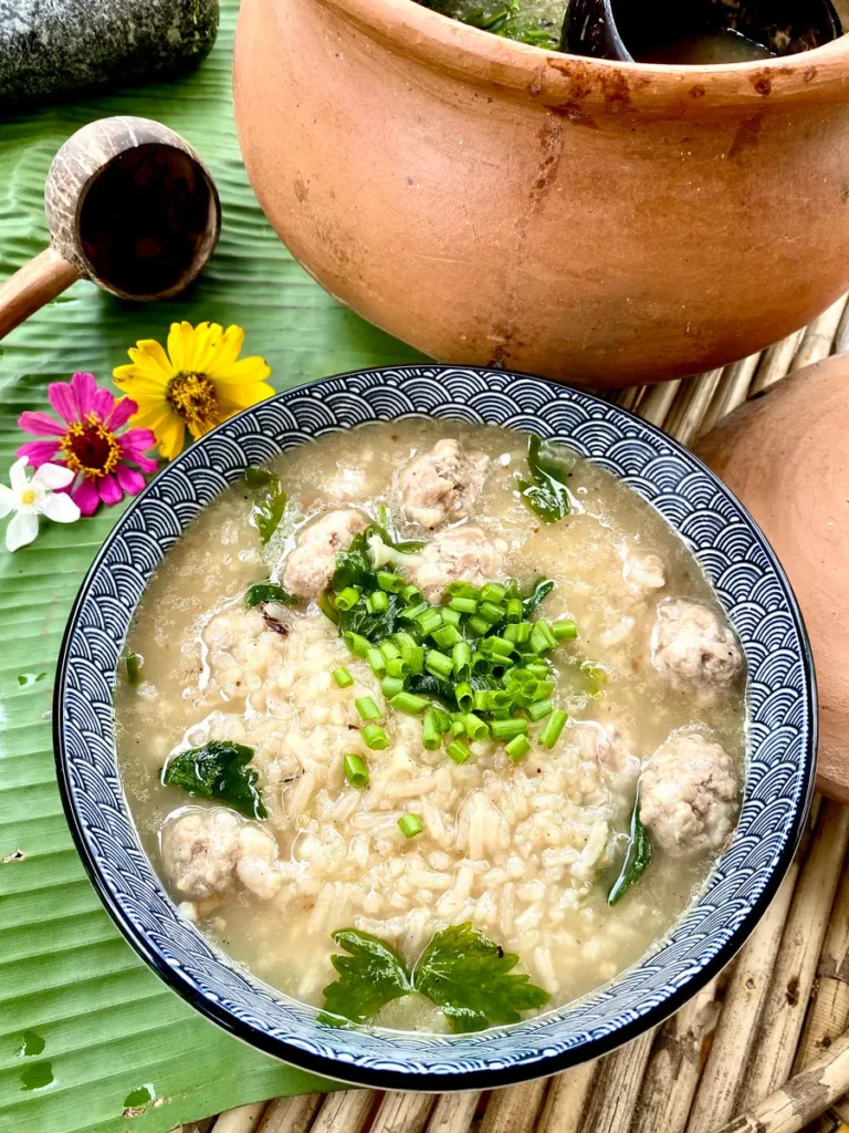 Top-down view of Thai khao tom rice soup with pork meatballs, garnished with green onions and celery.