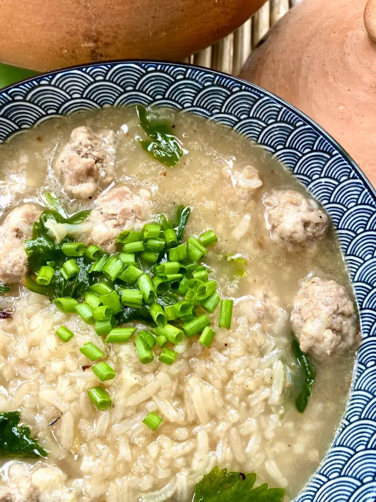 Thai rice soup served in a patterned bowl with chopped green onions and pork meatballs.