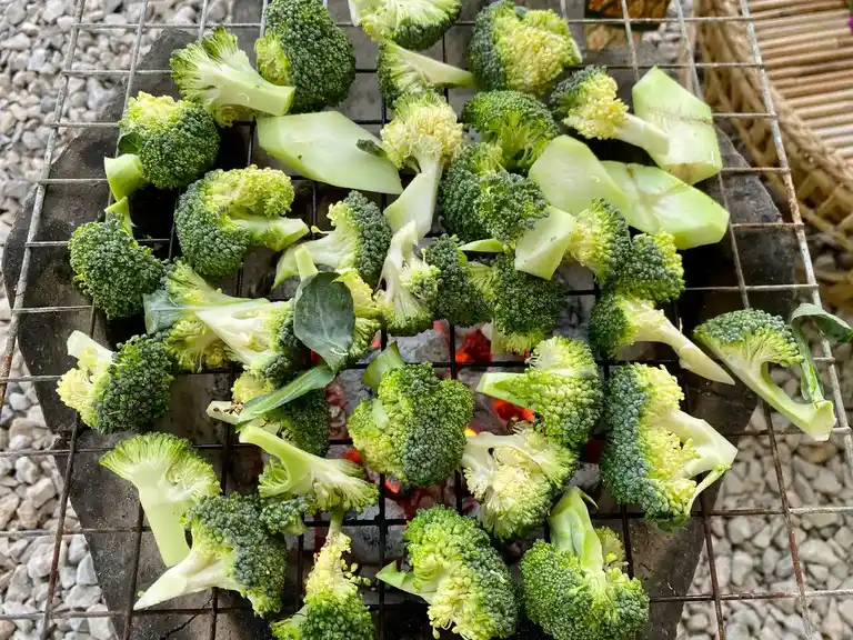 Broccoli florets being grilled over charcoal.