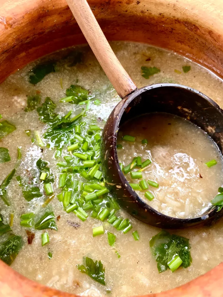 Close-up of khao tom Thai rice soup in a clay soup pot. There's also a large black soup spoon.