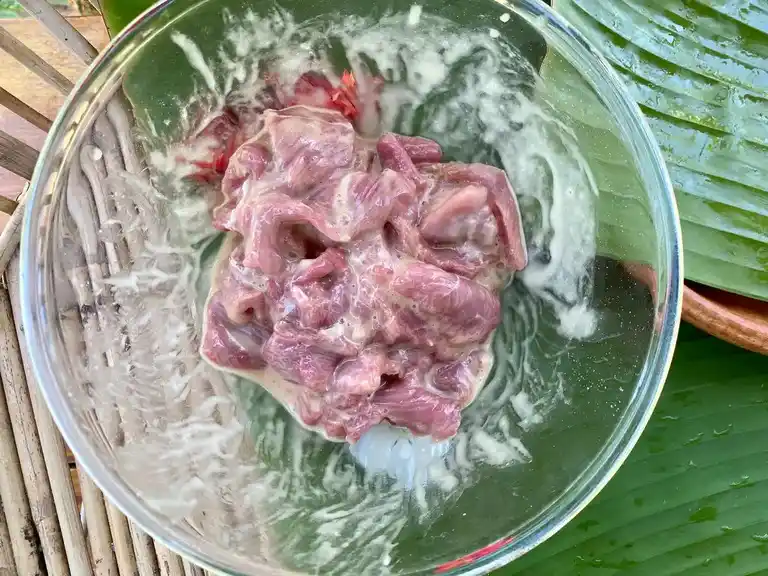 Sliced beef marinated in egg white, oyster sauce, and cornstarch in a clear mixing bowl.