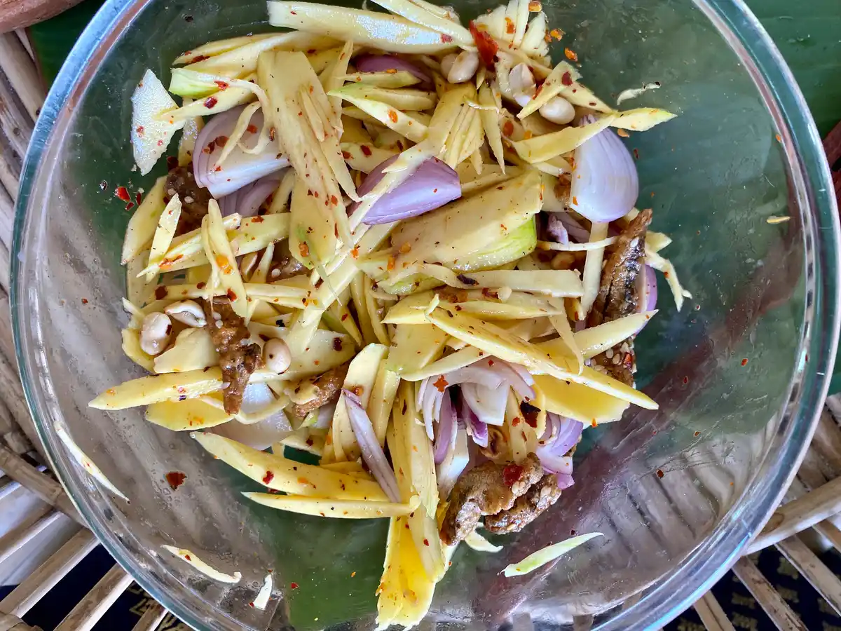 Overhead view of a large mixing bowl containing an Asian salad made with shredded mango and shallots.