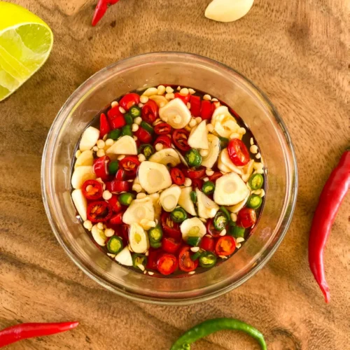 Prik nam pla prepared in a clear glass cup, with fresh red and green chilies, garlic, and fresh lime.