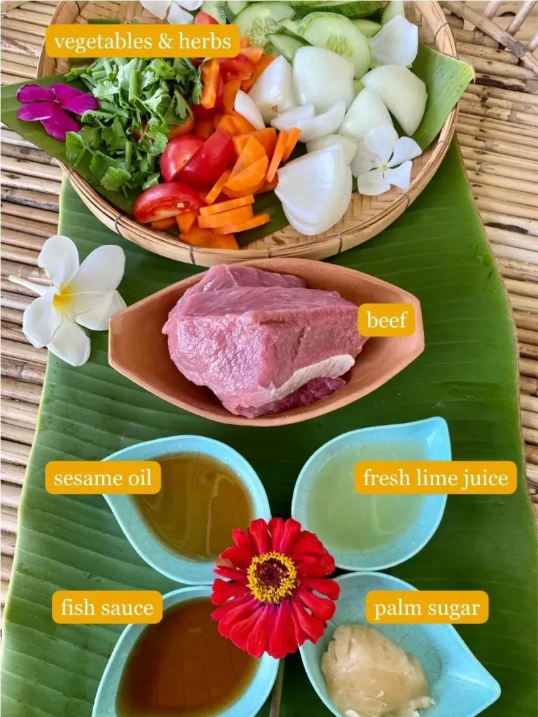 Recipe ingredients presented on a bamboo serving tray; vegetables & herbs, raw beef, fresh lime juice, sesame oil, fish sauce, and palm sugar. Most ingredients are in plastic cups or clay cups.